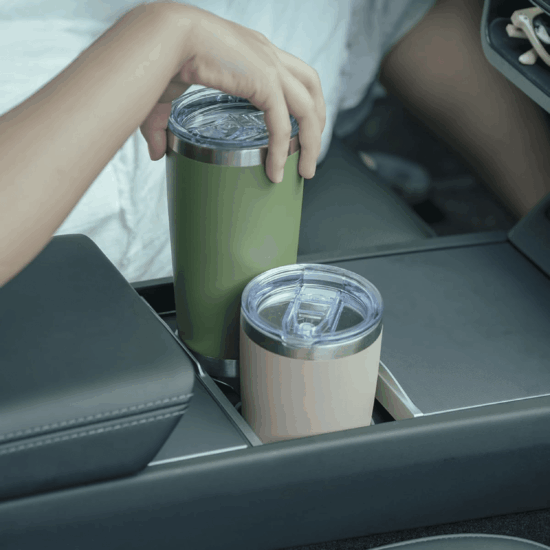 Two insulated tumblers in a car's cup holders, one held by a person.